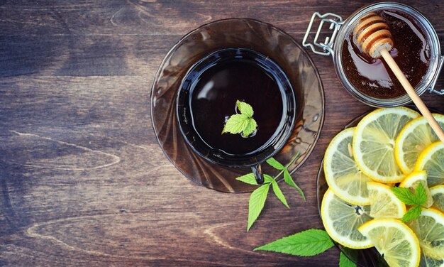 Thé au citron et à la menthe dans la nature. Une tasse de thé à la menthe chaud avec du citron et du miel en pot. Tranches de citron et une cuillère avec du miel pour du thé chaud.