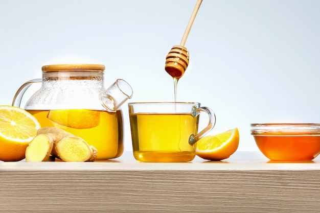 Thé au gingembre au citron et miel dans une tasse en verre sur table en bois.