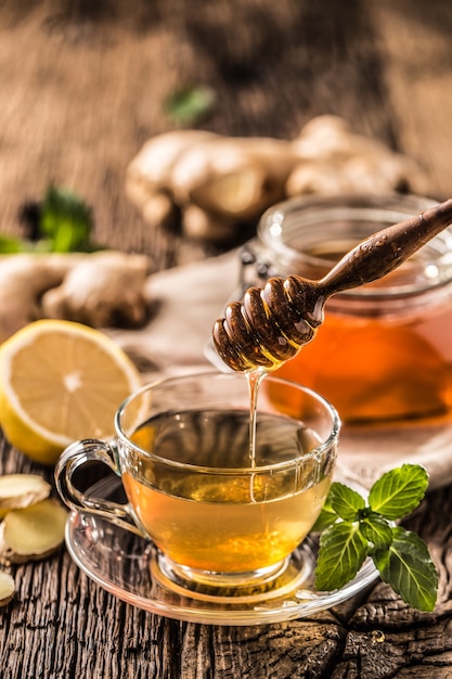 Thé au gingembre miel citron et feuilles de menthe sur table en bois.