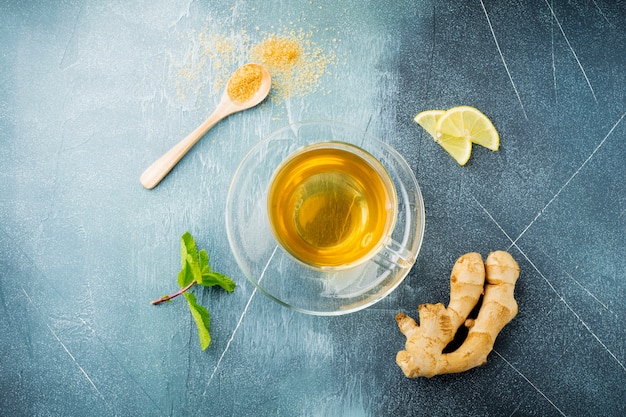 Thé au gingembre utile à la menthe, au citron et au sucre dans une tasse transparente sur un béton bleu.