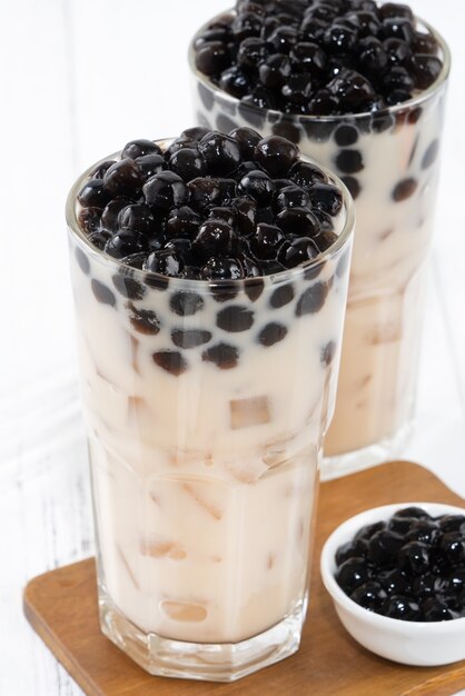 Thé au lait à bulles avec garniture de perles de tapioca, célèbre boisson taïwanaise sur fond de table en bois blanc dans un verre à boire, gros plan, espace pour copie