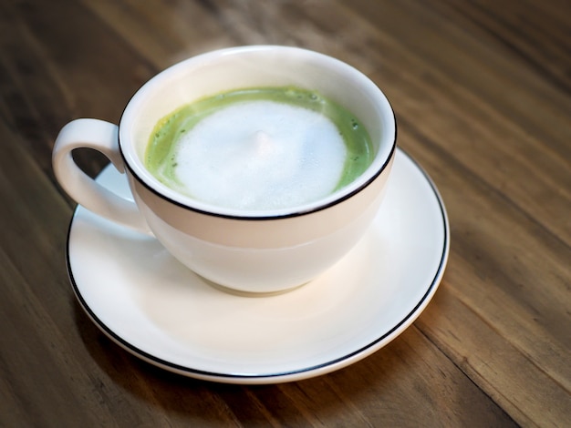 Photo thé au lait vert matcha chaud avec une tasse de mousse de lait sur la table en bois au café - boisson saine.