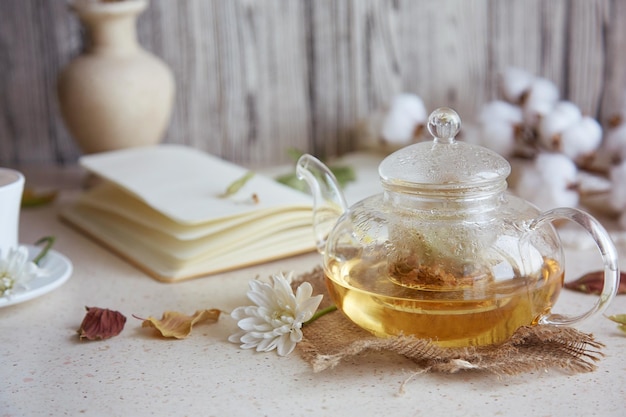 Thé au tilleul aux herbes esthétiques dans une théière avec une tasse de thé Feuilles de blé décorations d'automne en coton et carnet Atmosphère chaleureuse maison de détente