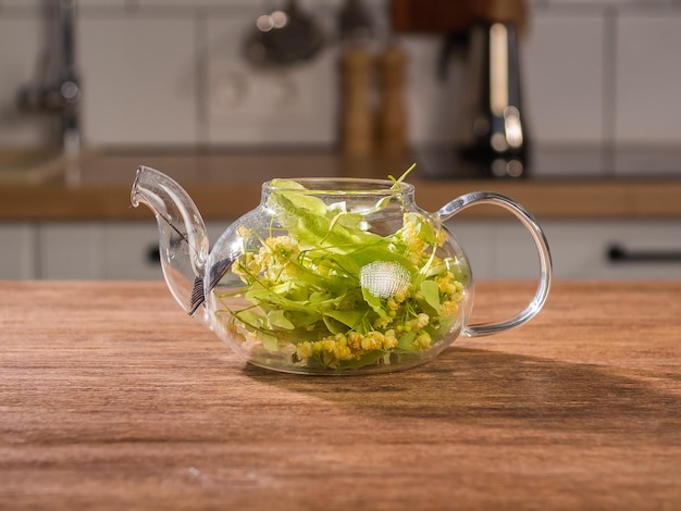 Thé au tilleul fraîchement infusé dans une théière se dresse sur une table de fond de cuisine traitement de tisane