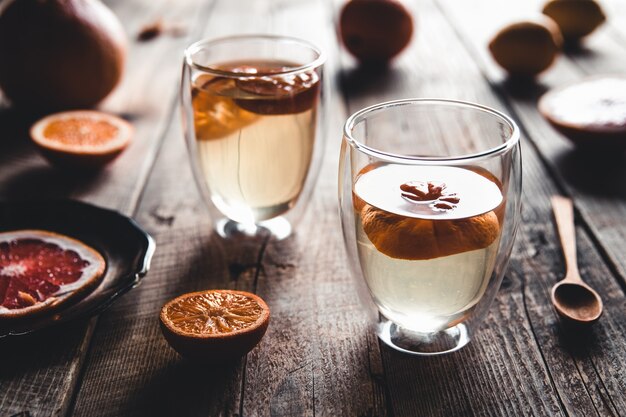 Thé aux agrumes dans une théière transparente et un verre, boisson saine sur un fond en bois.