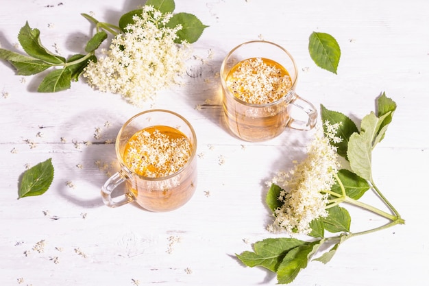 Thé aux fleurs de sureau. Boisson d'été rafraîchissante, concept de mode de vie sain. Lumière dure à la mode, ombre sombre. Vieux fond de planches de bois blanc, vue de dessus