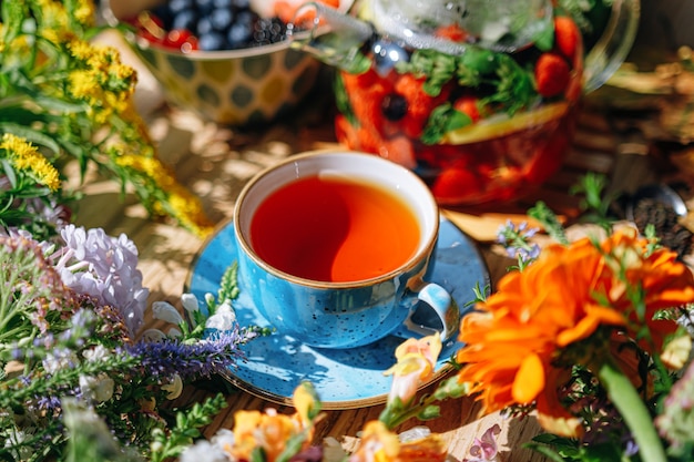 Thé aux fruits aromatiques naturels dans une théière transparente et dans une tasse parmi les baies et les fleurs. thé aromatique réchauffant avec un arôme profond de baies et de fleurs sauvages.