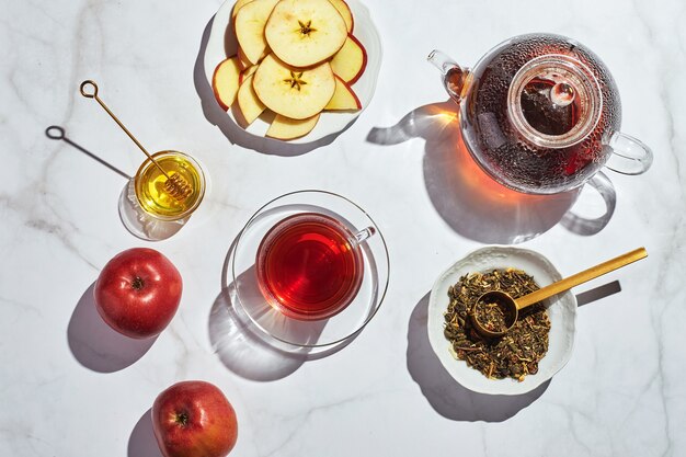 Thé aux fruits avec pommes et thym et miel dans une théière et une tasse en verre