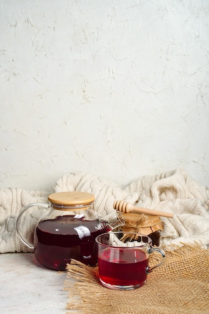 Thé aux fruits rouges avec du miel dans une théière transparente avec un pot et une cuillère pour le miel Fond de maison confortable avec espace de copie Photo de haute qualité