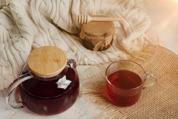 Thé aux fruits rouges avec du miel dans une théière transparente avec un pot et une cuillère pour le miel Fond de maison confortable Photo de haute qualité