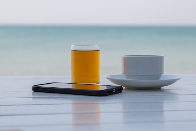 Thé café avec un téléphone intelligent sur la table en bois blanche sur le fond de la plage