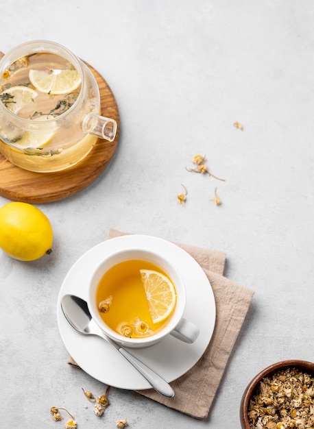 Thé à la camomille avec du citron dans une tasse blanche et une théière avec des fleurs sur un fond clair Le concept d'une boisson de désintoxication saine pour la santé et le sommeil