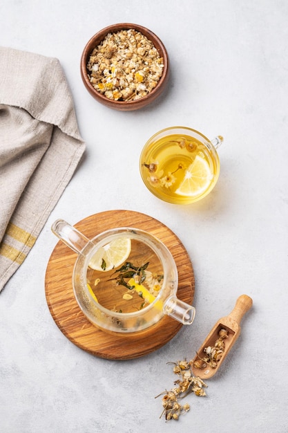 Thé à la camomille avec du citron dans une tasse en verre et une théière avec des fleurs sur un fond clair Le concept d'une boisson saine pour la santé et le sommeil