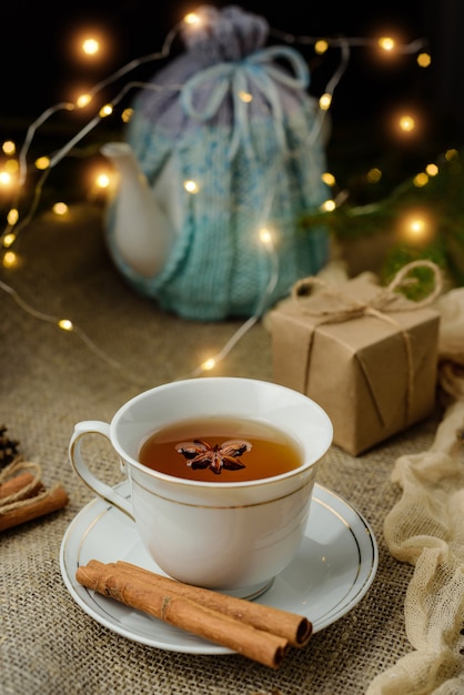 Thé à la cannelle sur une table décorée de guirlandes et de cadeaux. Soirée cosy à la maison.