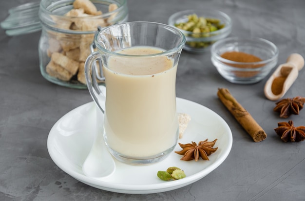 Thé chaud au lait, cannelle, cardamome, anis et autres épices, thé masala indien dans un verre sur fond sombre.