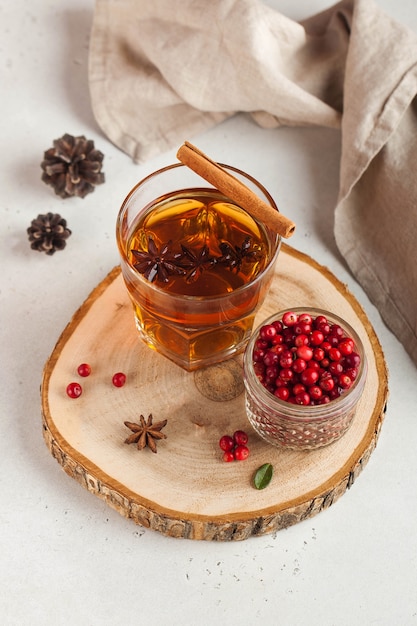 Thé chaud aux épices, pommes et baies de canneberge dans une tasse en verre transparent sur un support en bois.