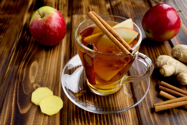 Thé chaud aux pommes, cannelle et gingembre dans la tasse en verre sur la surface en bois brun. Boisson saine.