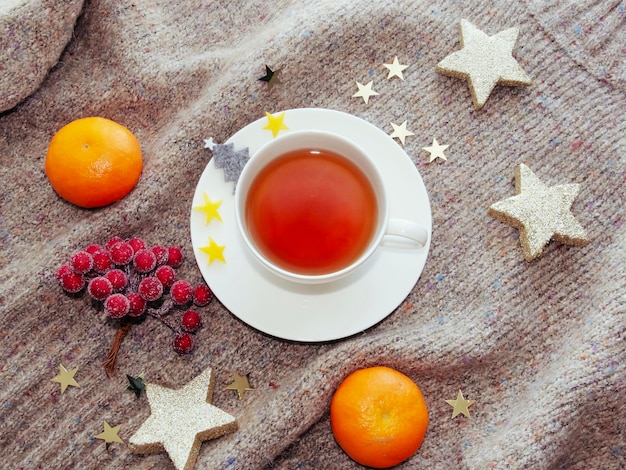 thé chaud dans une tasse blanche avec des mandarines et des décorations de Noël restant sur le pull chaud et confortable