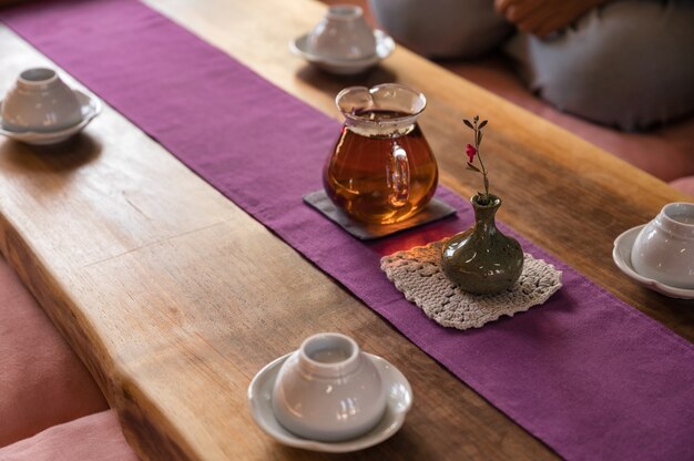 Thé chaud dans une théière en verre avec une fleur dans un vase et une tasse sur une table en bois