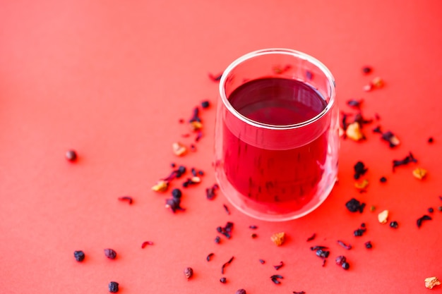 Thé chaud d'hibiscus dans un verre transparent à double fond sur fond rouge