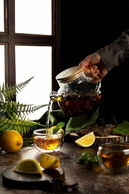 Photo le thé à la crème est versé d'une théière en verre dans une petite tasse de thé noir au citron et à la menthe