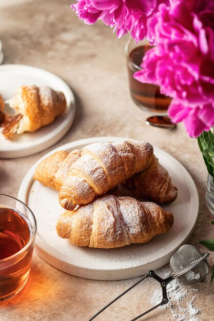 Thé de croissants frais et fleurs de pivoines roses pour le petit déjeuner sur fond marron avec espace de texte