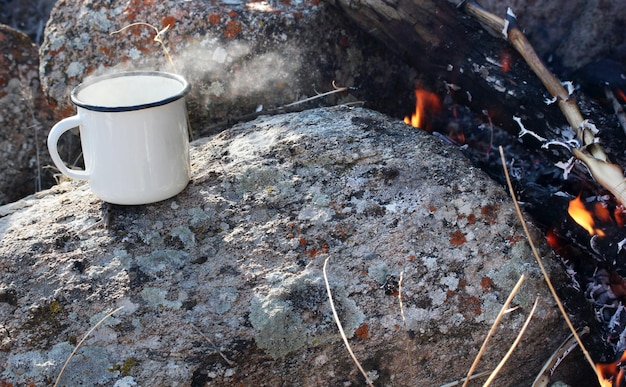 Le thé dans une tasse en métal se réchauffe sur la pierre au feu de joie