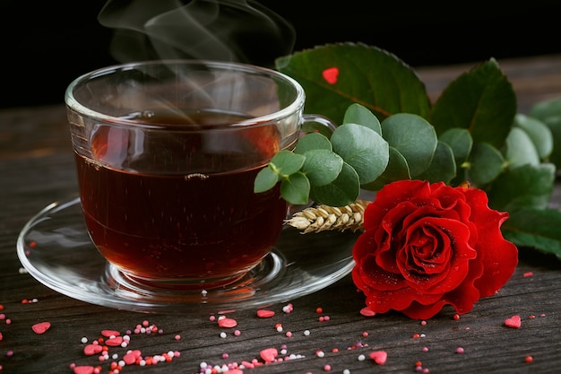 Thé dans une tasse transparente, bonbons de couleur et une rose rouge sur dark