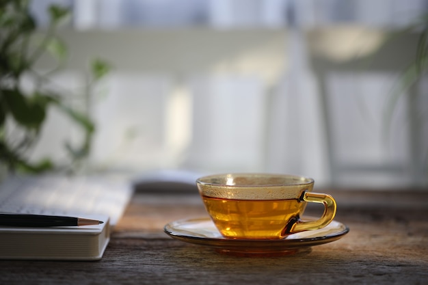 Thé dans une tasse en verre transparent sur une table en bois avec carnet et stylo