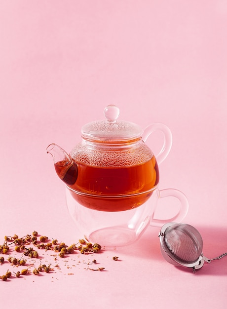 Thé dans une théière en verre sur fond rose et filtre infuseur en métal