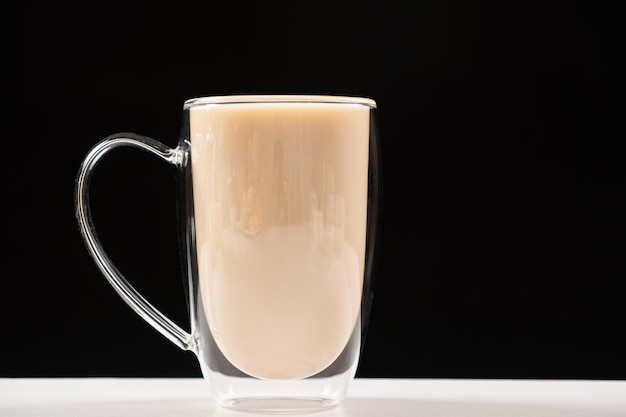 Thé avec du lait dans une tasse en verre à double fond sur un fond blanc et noir