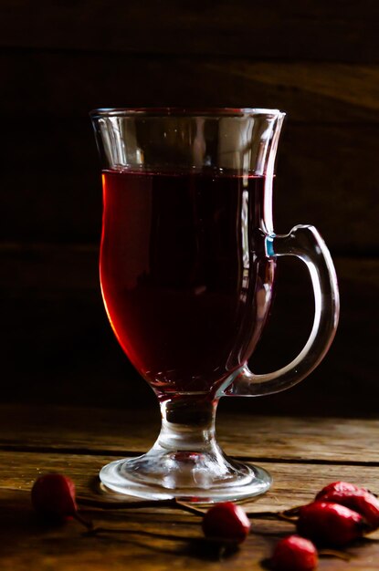 Thé d'églantier dans une tasse en verre sur un fond en bois.