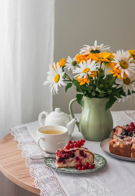 Thé d'été une tasse de thé vert un morceau de tarte aux baies une cruche avec des fleurs de jardin sur une table ronde dans le salon