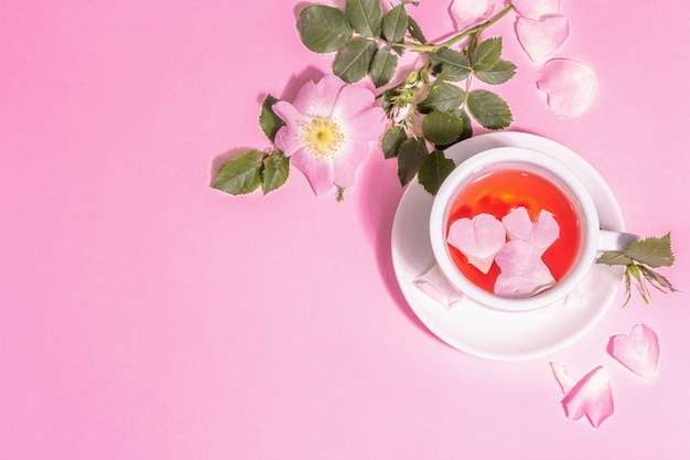 Thé de fleurs d'églantier. Boisson vitaminée d'été, lumière dure, ombre sombre. Fond pastel rose, vue de dessus