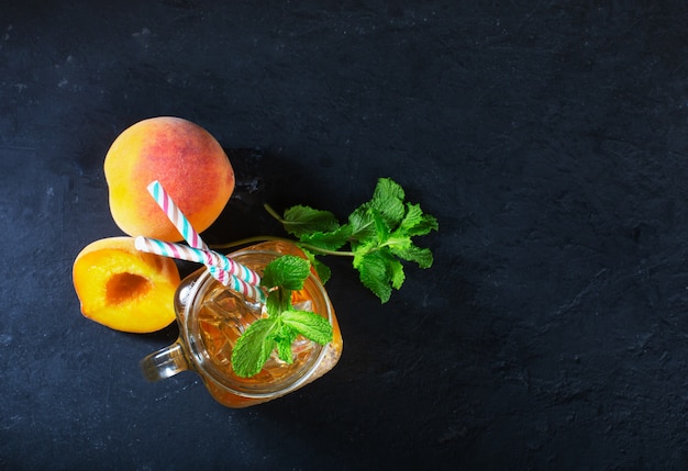 Thé glacé à la pêche sur fond sombre avec de la menthe et de la glace, bonne boisson pour la saison chaude d'été