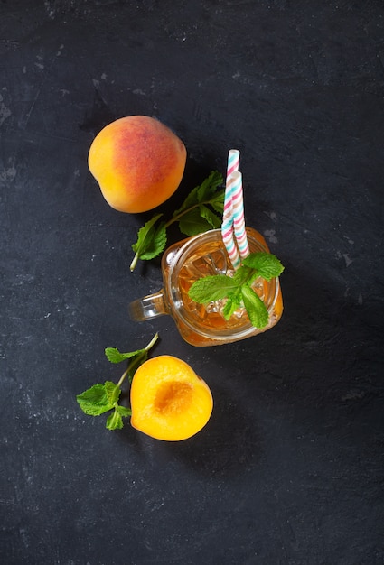 Thé glacé à la pêche sur fond sombre avec de la menthe et de la glace, bonne boisson pour la saison chaude d'été