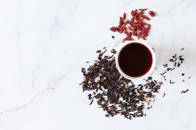 Thé d'hibiscus rouge dans une tasse en verre et vue de dessus de baies de goji sur fond de marbre blanc