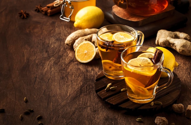 Thé d'hiver noir chaud avec gingembre, miel, citron et épices Boisson de rappel immunitaire dans une tasse en verre sur fond de table en bois rustique espace de copie