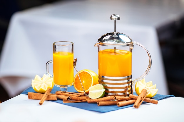 Thé jaune d'agrumes lumineux dans une tasse et une presse française à la cannelle