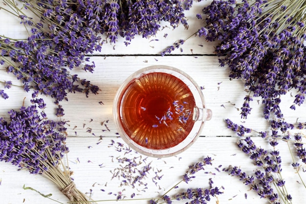 Thé à la lavande Vue de dessus du thé à la lavande apaisant dans une tasse en verre avec des pétales de fleurs de lavande sur fond de bois blanc