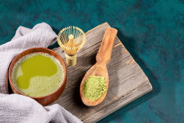 Thé Matcha et poudre de matcha sur planche de bois sur fond d'émeraude.