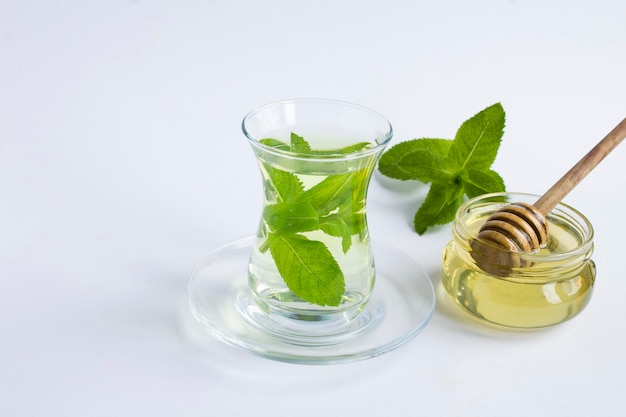 Thé à la menthe et au miel dans la tasse en verre sur fond blanc Espace de copie libre