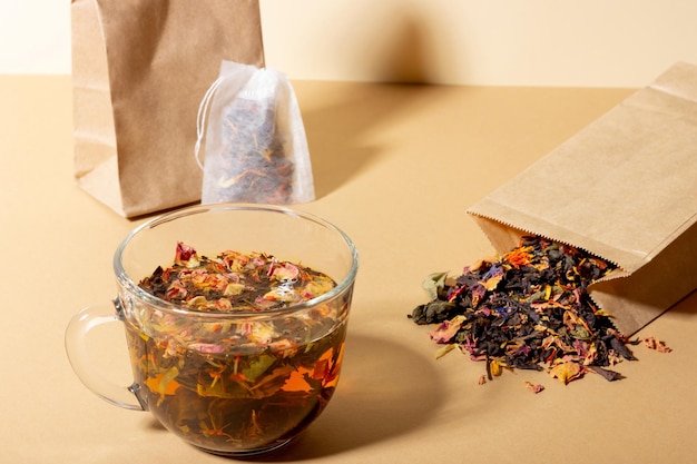 Thé noir à base de plantes et de fruits infusé dans une tasse transparente Thé à infuser dans des sachets de thé Le concept d'une boisson saine et naturelle Sachets de thé sur fond beige