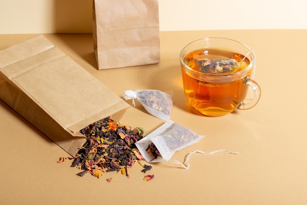 Thé noir à base de plantes et de fruits infusé dans une tasse transparente Thé à infuser dans des sachets de thé Le concept d'une boisson saine et naturelle Sachets de thé sur fond beige