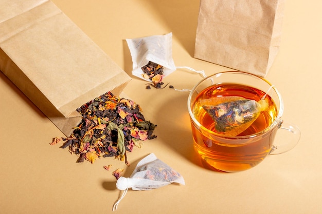 Thé noir à base de plantes et de fruits infusé dans une tasse transparente Thé à infuser dans des sachets de thé Le concept d'une boisson saine et naturelle Sachets de thé sur fond beige