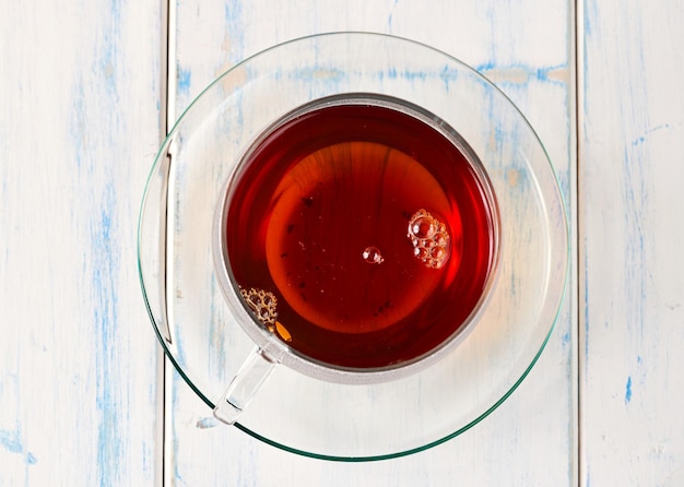 Thé noir dans une tasse en verre sur une table en bois blanche.