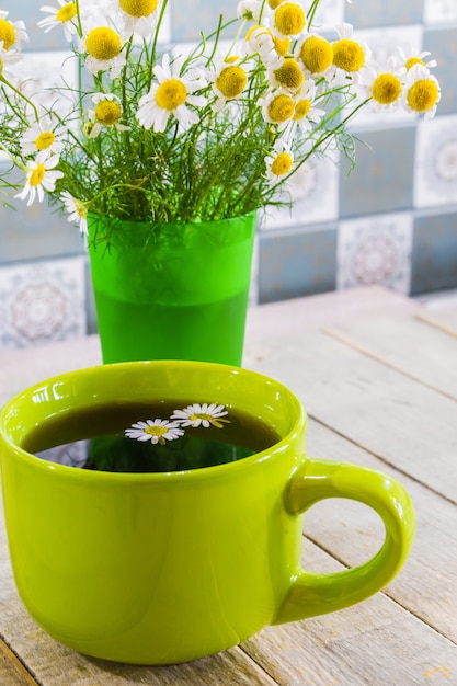 Thé noir dans une tasse verte sur fond de bois et camomille