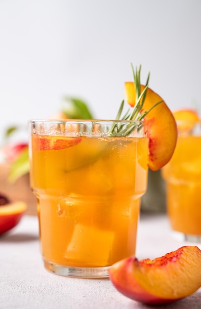 Thé rafraîchissant à la pêche avec de la glace et du romarin en gros plan Boisson végétarienne saine et froide faite maison sur un fond clair avec des fruits frais