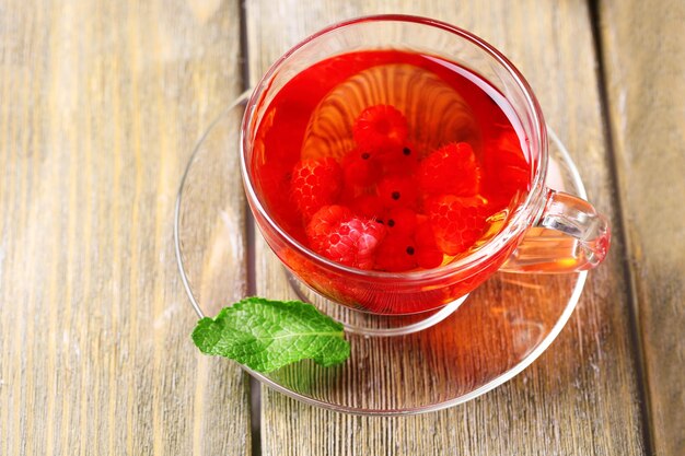 Thé rouge aux fruits avec des baies sauvages dans une tasse en verre sur fond de bois