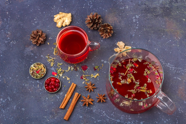 Thé rouge dans une tasse en verre et une théière parmi les pétales de feuilles de thé sec et les pommes de pin